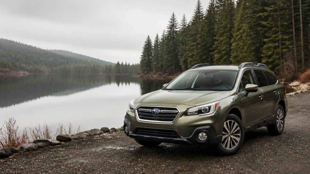 Green 2017 Subaru Outback parked beside a calm forest lake, highlighting its outdoor and all-weather capability