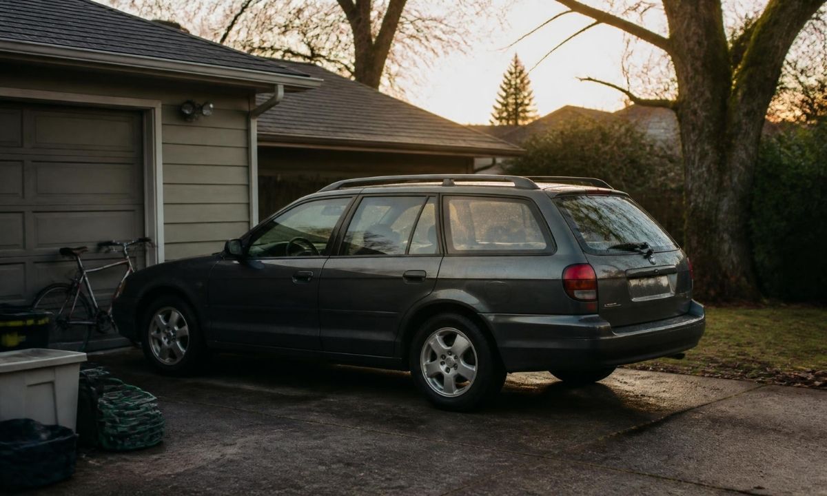 Older Subaru Outback wagon parked beside a garage at sunset, showing long-term ownership