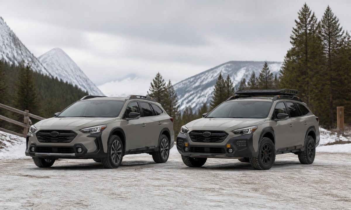 Two Subaru Outbacks parked side by side on packed snow with snow-covered mountains behind